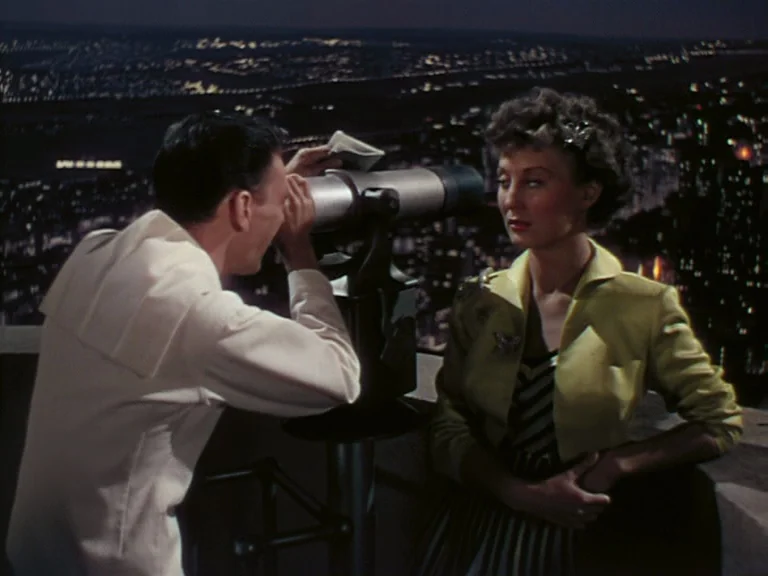 On The Town (1949) movie still: medium — An outdoor viewing platform at night overlooking a blurred expanse of urban city lights. A man peers…