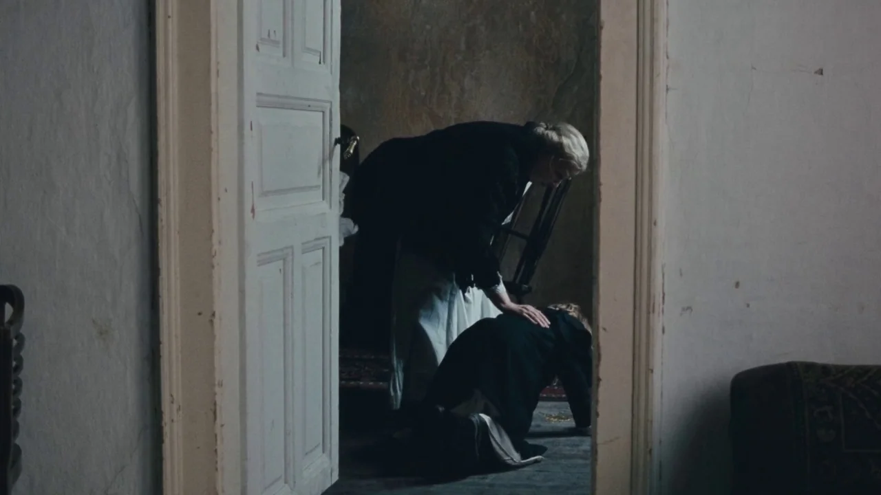 Childhood of a Leader (2015) movie still: medium — An interior space with a partially open wooden door leading to an adjacent room. An elderly woman…