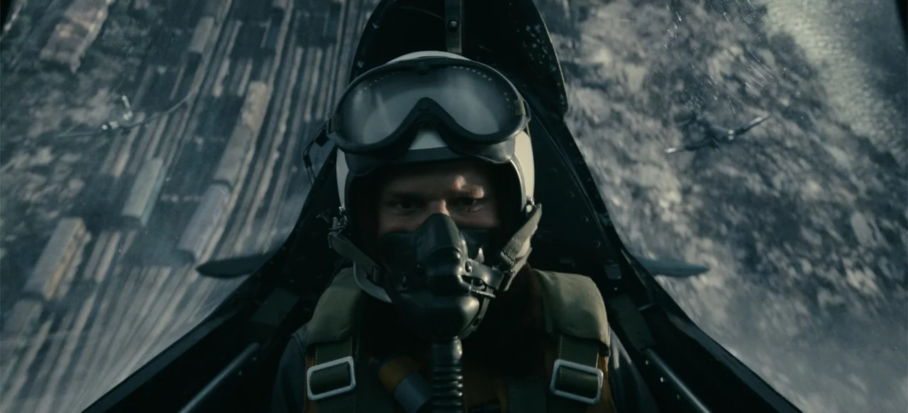 Devotion (2022) movie still: closeup — A pilot sits inside the glass canopy of a high-speed fighter aircraft. The pilot gazes ahead while flying…