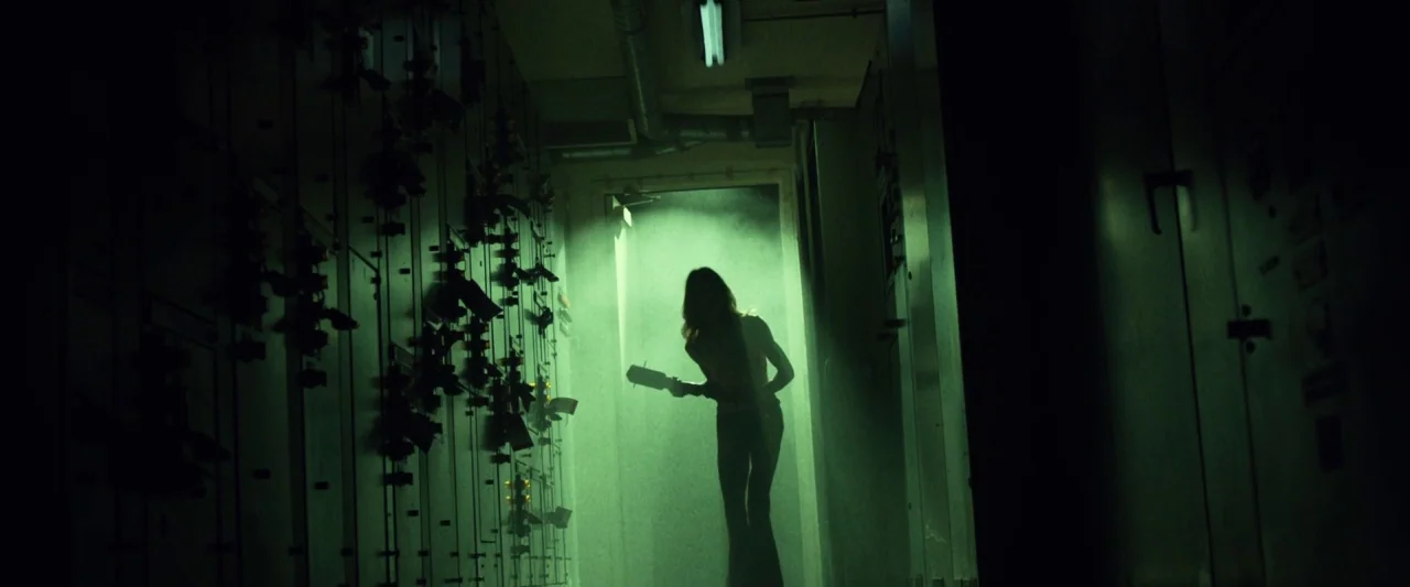 31 (2016) movie still: wide — A dark utility room features rows of metallic electrical cabinets lining the side walls. A person stands in an open…