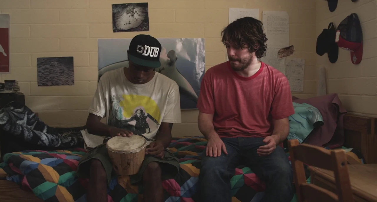 Short Term 12 (2013) movie still: medium — A student dormitory with cinder block walls decorated with various posters and notes. Two men sit on a…