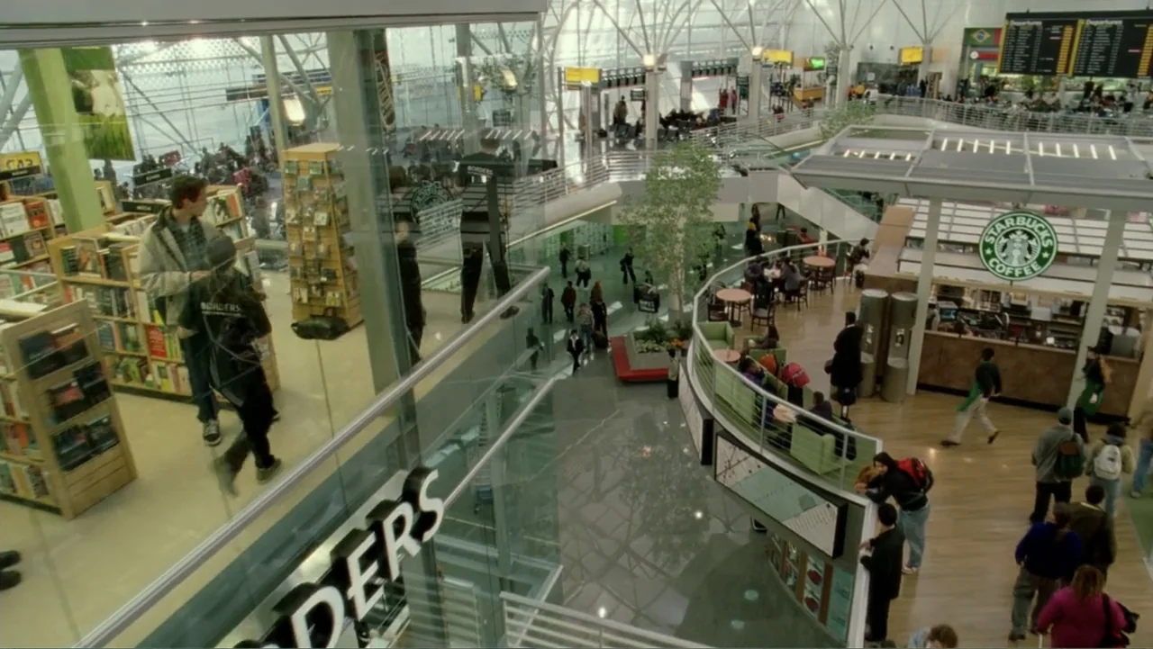 The Terminal (2004) movie still: wide — A spacious, multi-level modern airport terminal features glass walls and a central atrium. Pedestrians and…