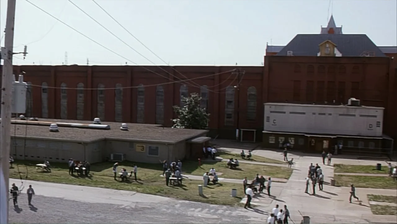 Against the Wall (1994) movie still: wide — A sprawling prison complex features large red brick walls and low-rise concrete buildings. Inmates…