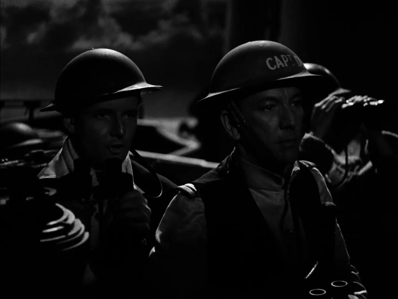 In Which We Serve (1942) movie still: medium — A dark military environment with soldiers wearing Brodie helmets in a dimly lit space. The officers…