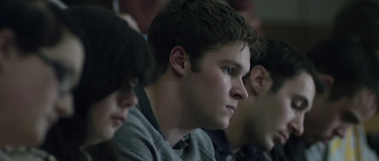 What Richard Did (2012) movie still: medium — A group of young adults sit in rows within a dark, tiered lecture hall. The main subject focuses his…