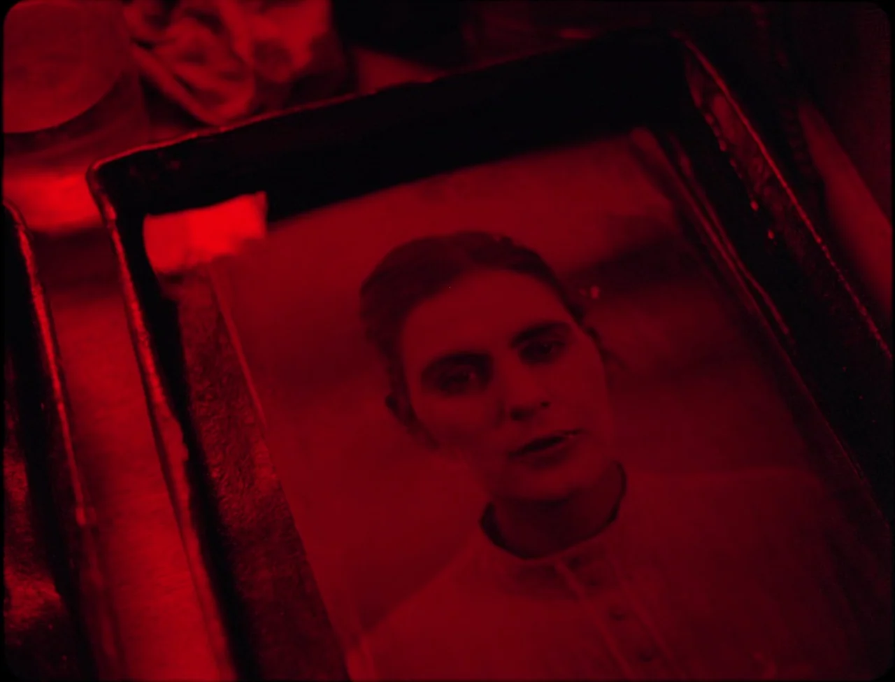 Godland (2022) movie still: closeup — A darkroom with a single photographic print resting in a black developing tray. The woman in the photograph…
