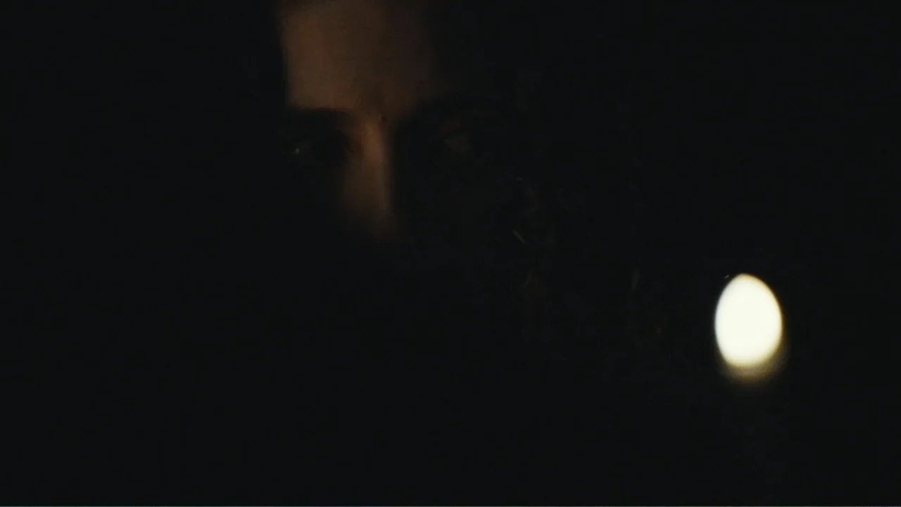 Demon in the White House (2021) movie still: closeup — An interior space is almost completely obscured by deep shadows at night. A face is partially…