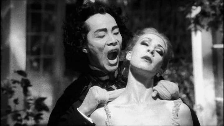 Dracula: Pages from a Virgin’s Diary (2002) movie still: medium — An outdoor area with blurred white architectural elements and dark foliage in the…