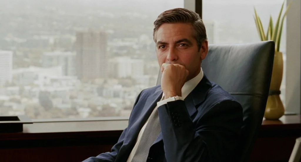 Intolerable Cruelty (2003) movie still: medium — A high-rise executive office features a large window overlooking a blurred city skyline. A man…