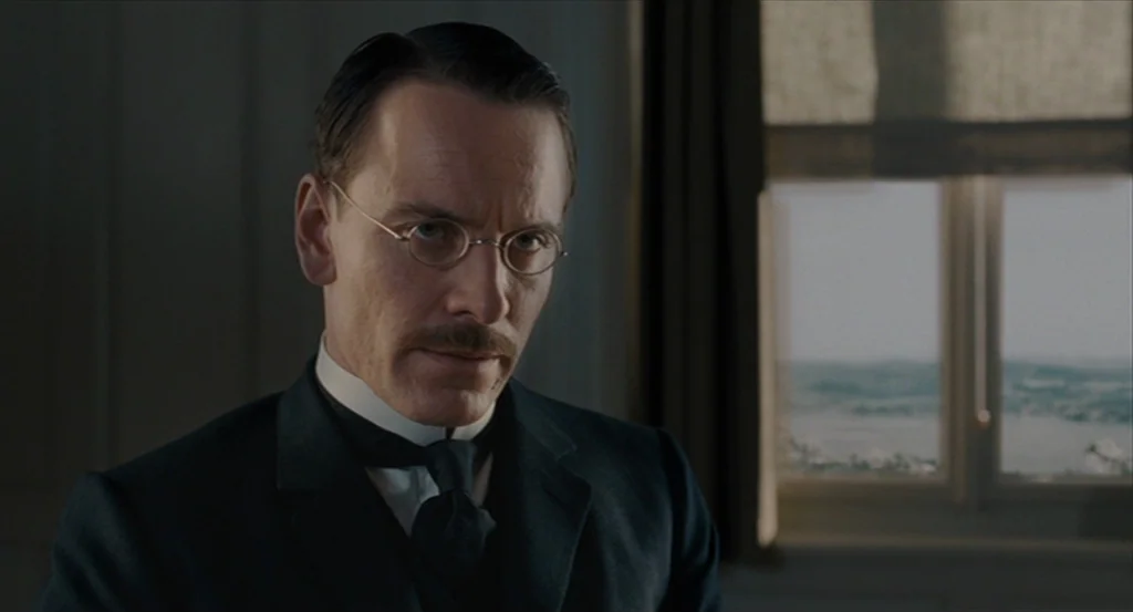 A Dangerous Method movie still: closeup — A man stands inside a room next to a window with a view. He wears formal period-appropriate attire…