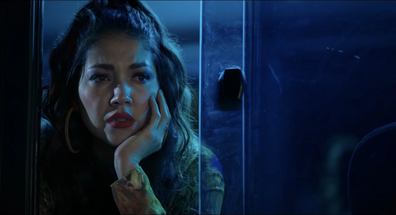 The Beauty and the Moody (2022) movie still: closeup — The interior of a vehicle at night with blue light reflecting through the window. A young…