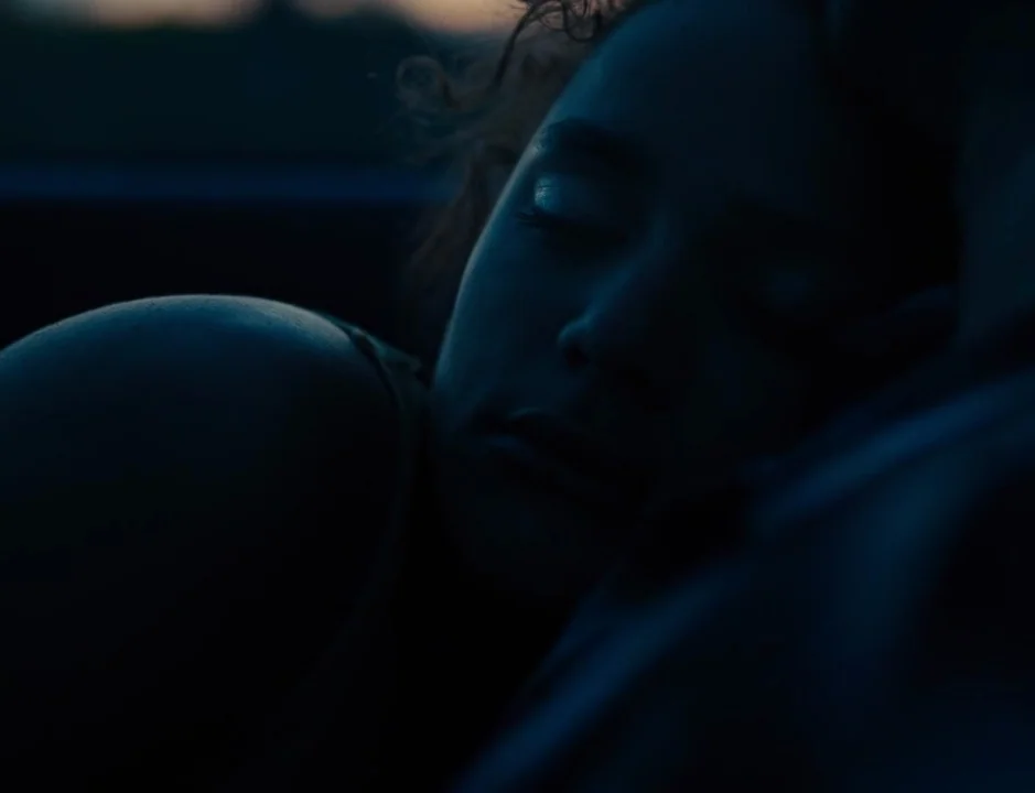 American Honey (2016) movie still: closeup — A close-up view of a person resting in a dimly lit dark environment. The subject keeps their eyes…