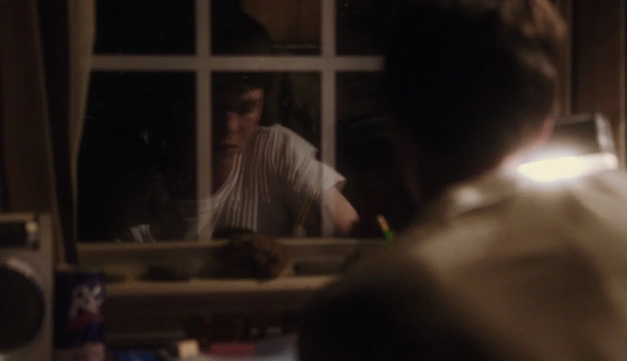 The Perks of Being A Wallflower (2012) movie still: medium — A dimly lit interior space features a window displaying a reflection of a person. The…