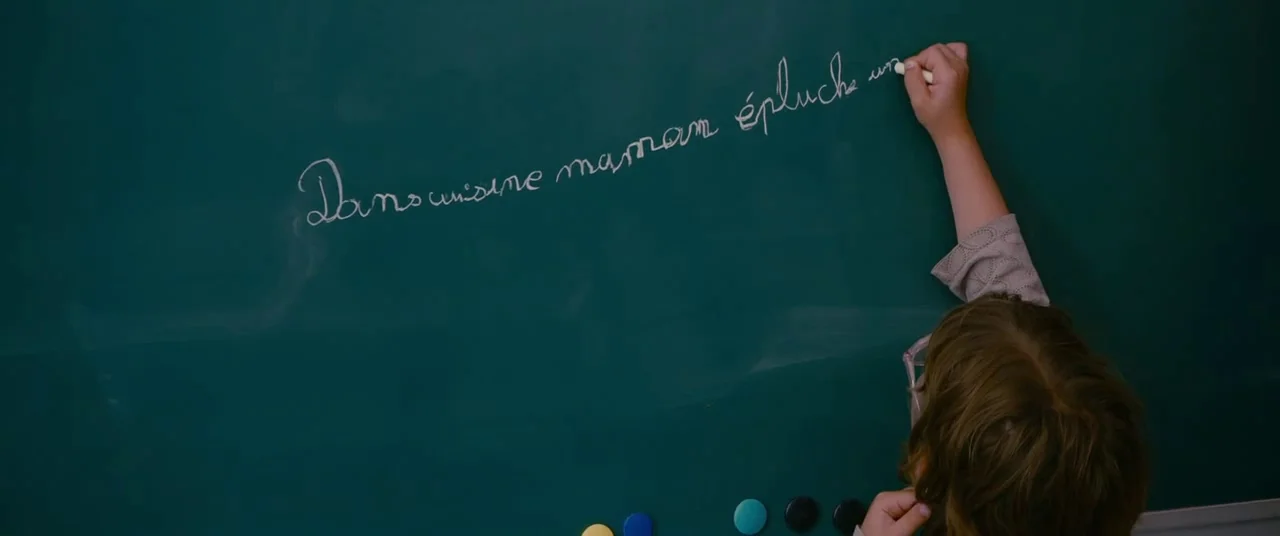 Blue Is The Warmest Colour (2013) movie still: medium — A green chalkboard features handwritten French text in white chalk. A child stands facing…