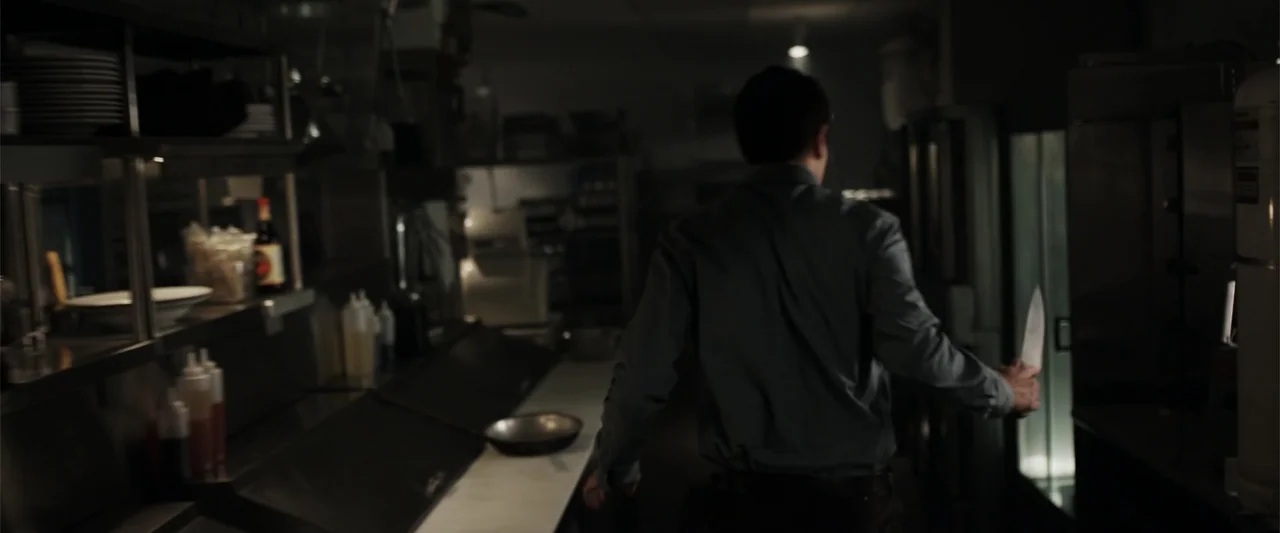 Final Destination 5 (2011) movie still: medium — A dark restaurant back-of-house area with stainless steel surfaces and shelves. A man in a…