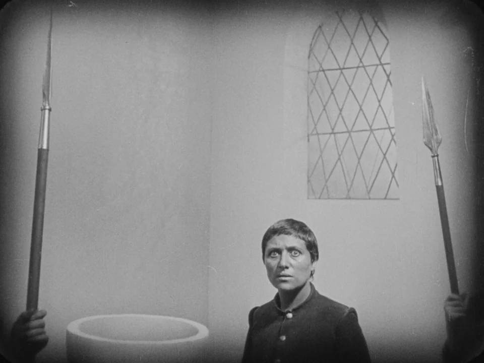 The Passion of Joan of Arc (1928) movie still: medium — A stark white stone room with a small high lattice window and rounded bowl. A woman stands…
