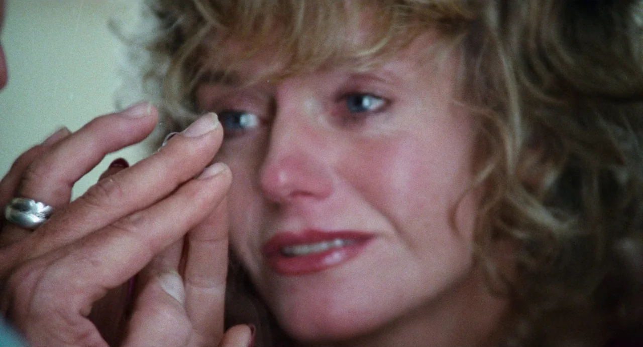 Out of the Blue (1980) movie still: closeup — An indoor setting shows a person's hand holding a contact lens up to a woman. The woman watches the…