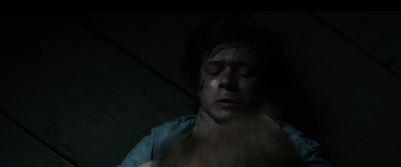 Strange but True (2019) movie still: closeup — An interior space with dark wooden planks serving as a base for the subject. A young male lies prone…