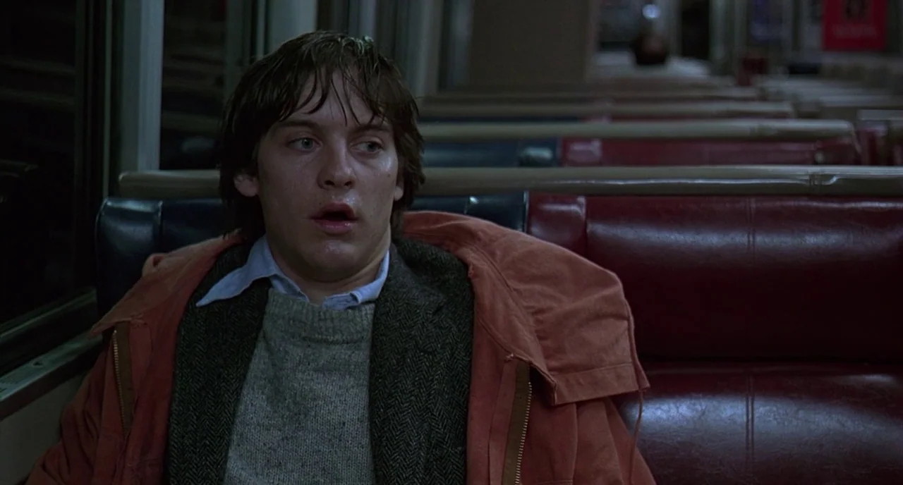 The Ice Storm (1997) movie still: medium — The interior of a subway car features rows of empty red vinyl seats at night. A young man sits in the…