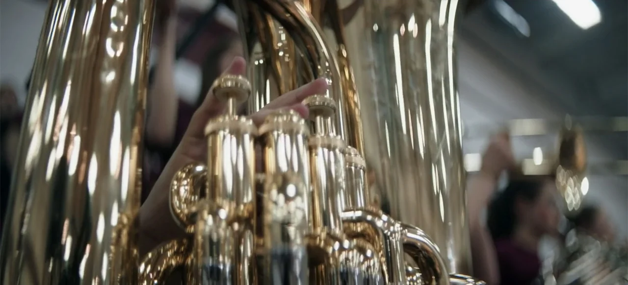 I Still See You (2018) movie still: closeup — A close-up view shows the polished brass valve assembly of a large wind instrument. A person's hand…