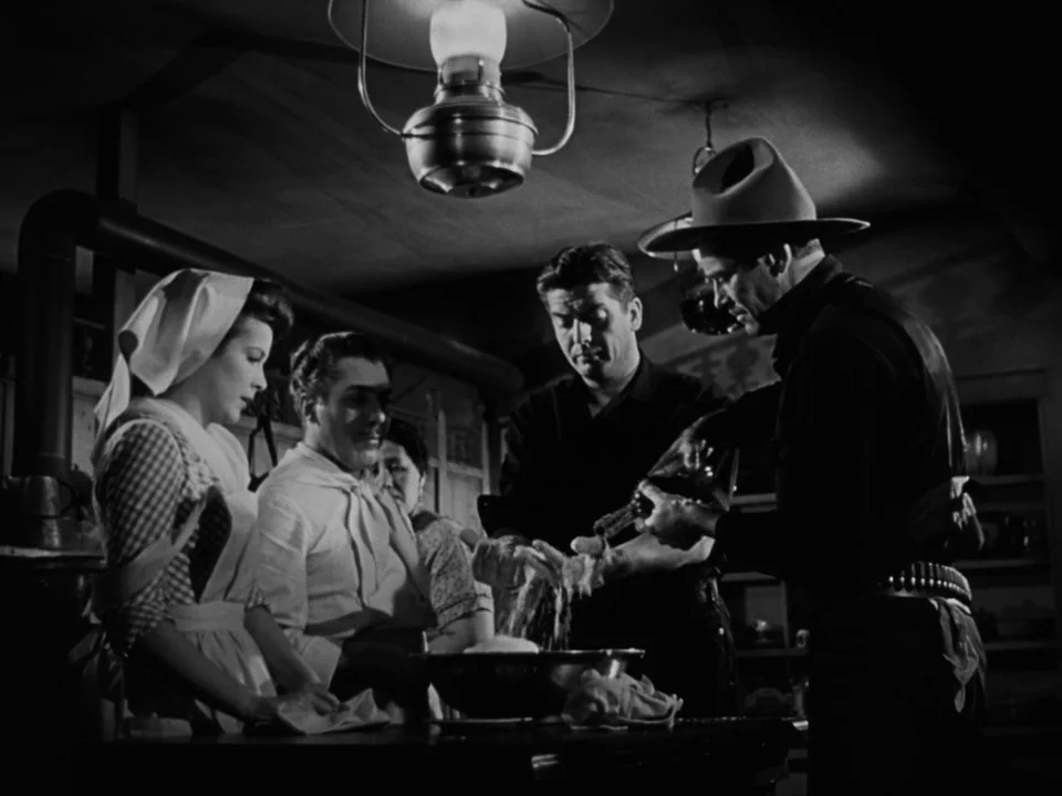My Darling Clementine (1946) movie still: medium — A dimly lit rustic room with heavy wooden furniture and a suspended oil lamp. Four people gather…