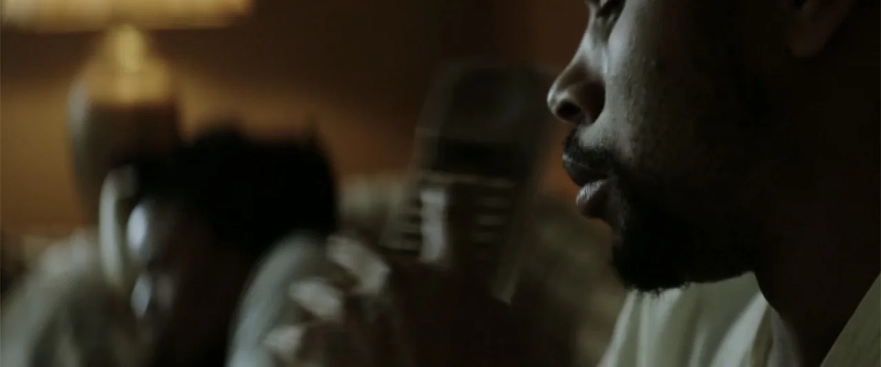 Crown Heights (2017) movie still: closeup — A dimly lit room contains a person holding a telephone receiver. A man in profile focuses on a…