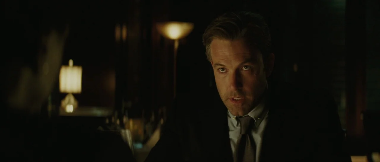 Suicide Squad (2016) movie still: medium — A dimly lit, upscale restaurant interior at night with dark wood-toned decor. A man in a suit speaks…