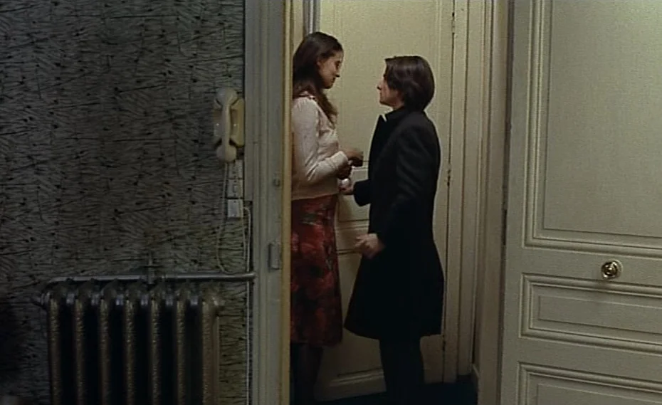 Bed & Board (1970) movie still: medium — A narrow apartment entryway features textured patterned wallpaper and a white paneled door. Two women stand…