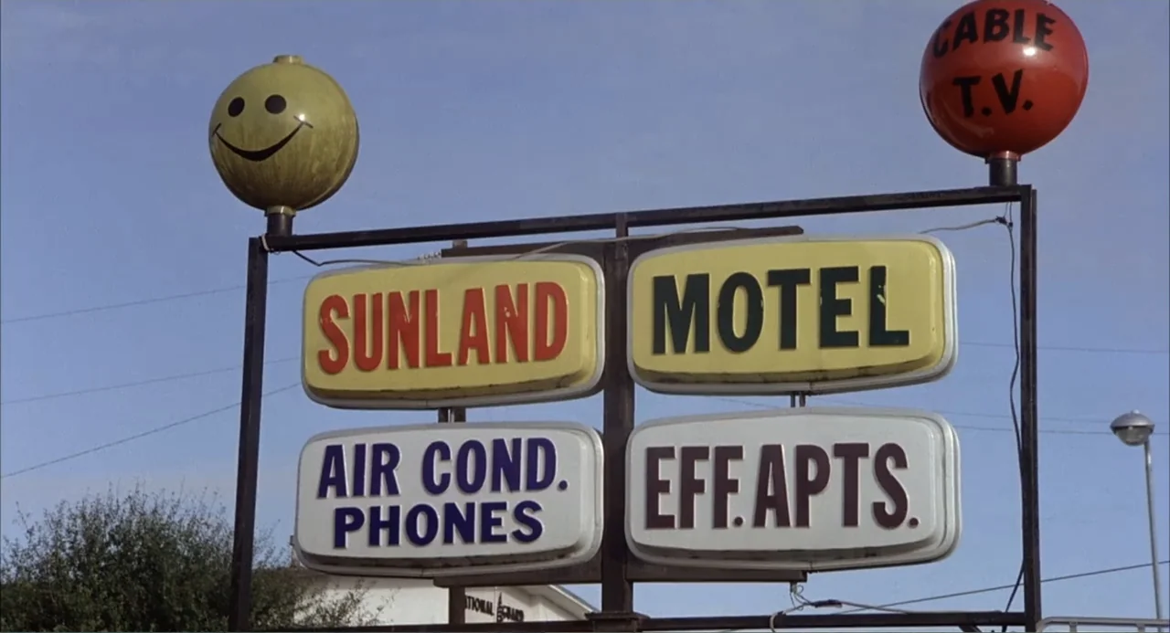 Empire of the Ants (1977) movie still: wide — A roadside motel sign with yellow, red, and white panels sits against blue sky. The sign features a…