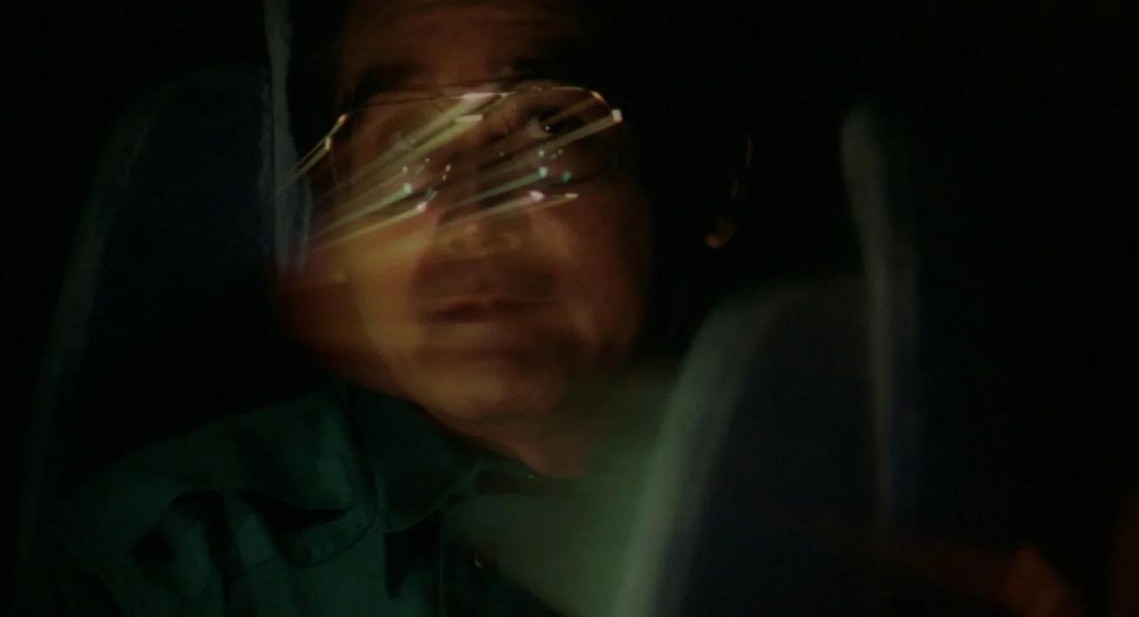 Godzilla vs. King Ghidorah (1991) movie still: closeup — The interior of a vehicle cabin at night with deep shadows surrounding the driver. An East…