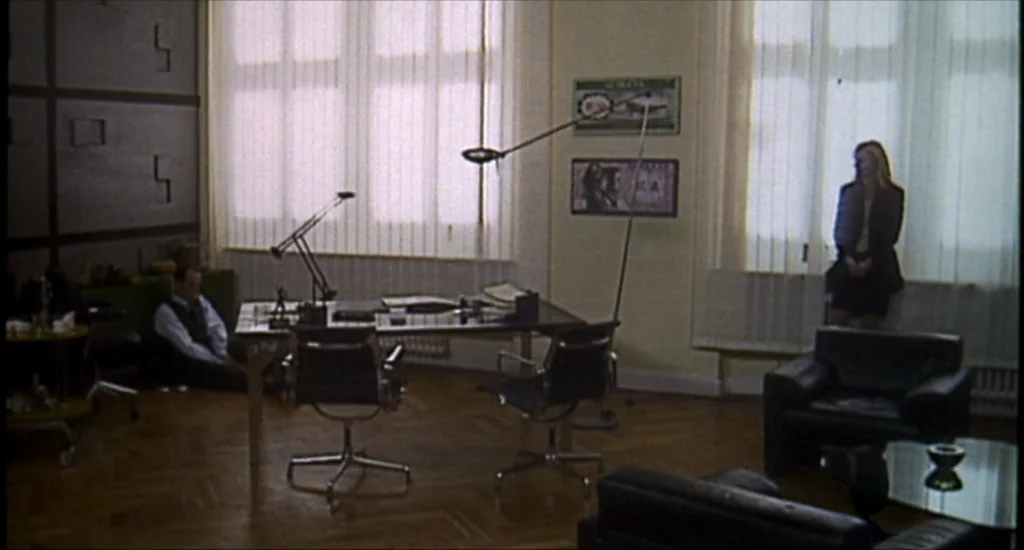 Run Lola Run (1998) movie still: wide — A corporate office features dark leather furniture, parquet wooden flooring, and large vertical blinds. One…