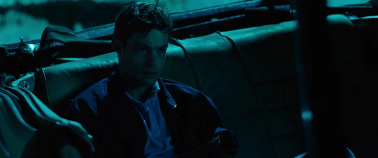Knife+Heart (2018) movie still: medium — The back seat of a vehicle at night has vinyl upholstery and a dark interior. A young man sits in the seat,…