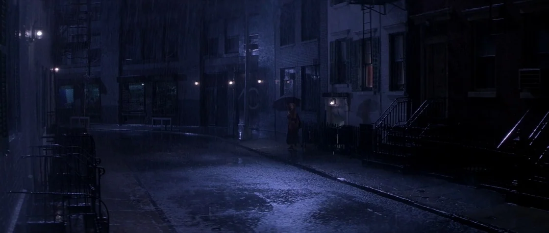 Carlito’s Way (1993) movie still: wide — A dark city street at night is saturated with heavy falling rain. A single figure holding an umbrella…