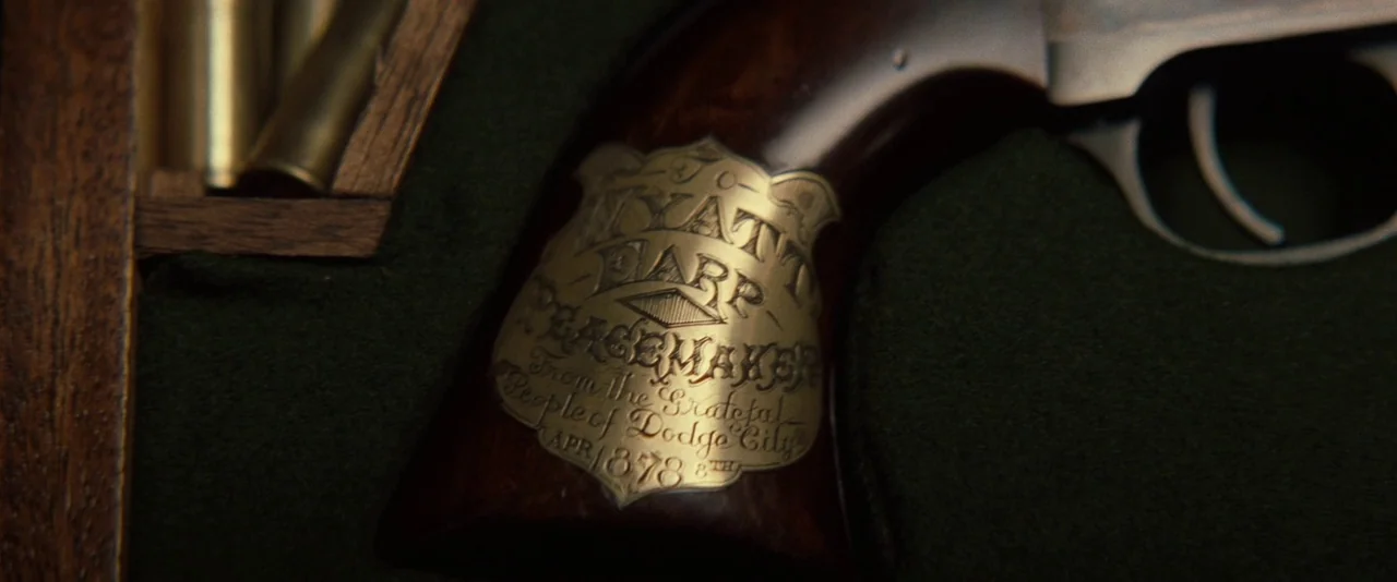 Tombstone (1993) movie still: closeup — A close-up of a Colt revolver resting in a velvet-lined wooden display case. The wooden grip features an…
