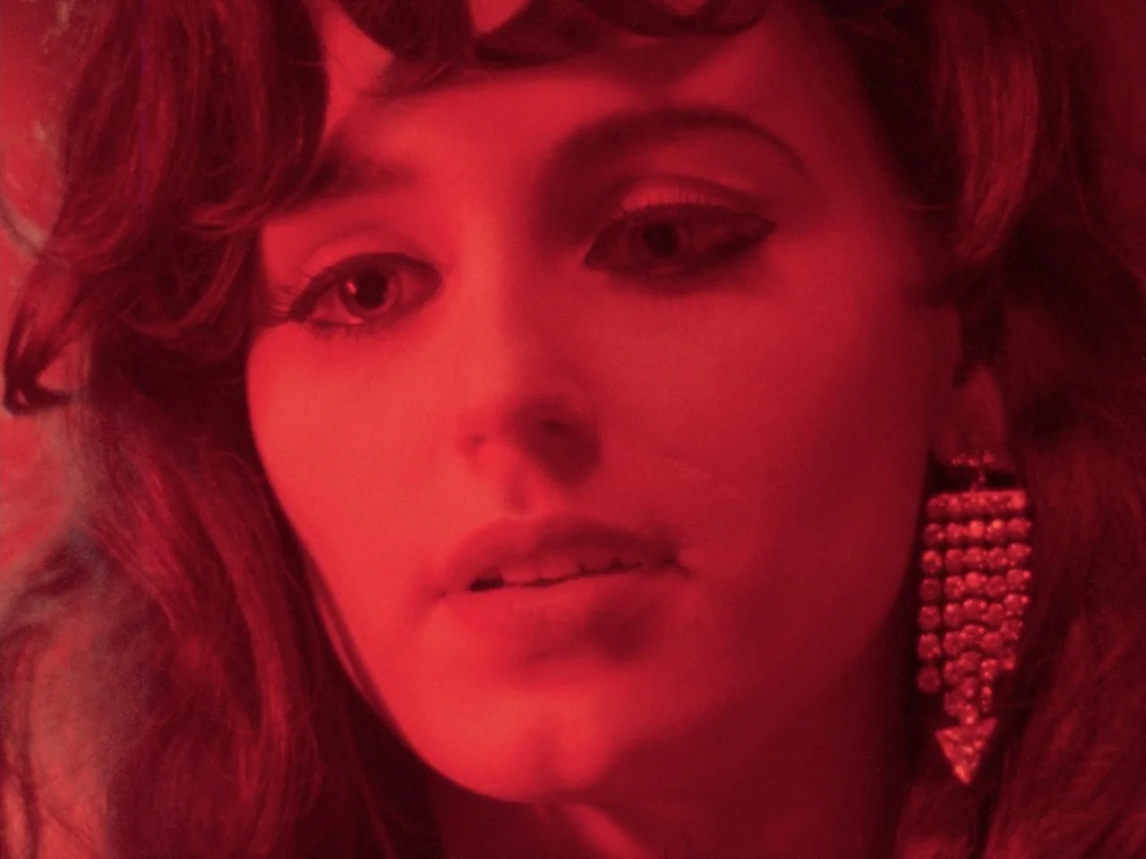 Decoder (1984) movie still: closeup — A woman's face is closely framed against an out-of-focus background. She wears a large decorative earring…