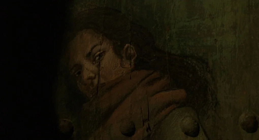 Furia (1999) movie still: closeup — A dark, heavily weathered green metal door features a worn mural of a face. The painted image depicts a person…