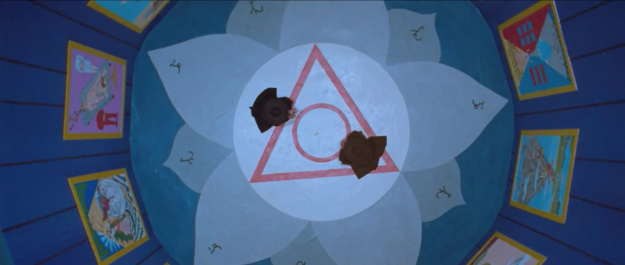 The Holy Mountain (1973) movie still: wide — A circular room features a large lotus-patterned floor painted with a red triangle. Two individuals sit…