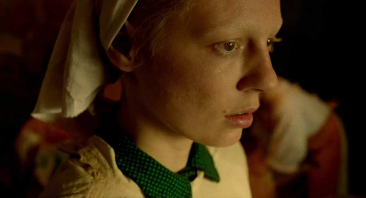 Beanpole (2019) movie still: closeup — A dimly lit interior space contains a young woman wearing a headscarf. She looks to the right side of the…
