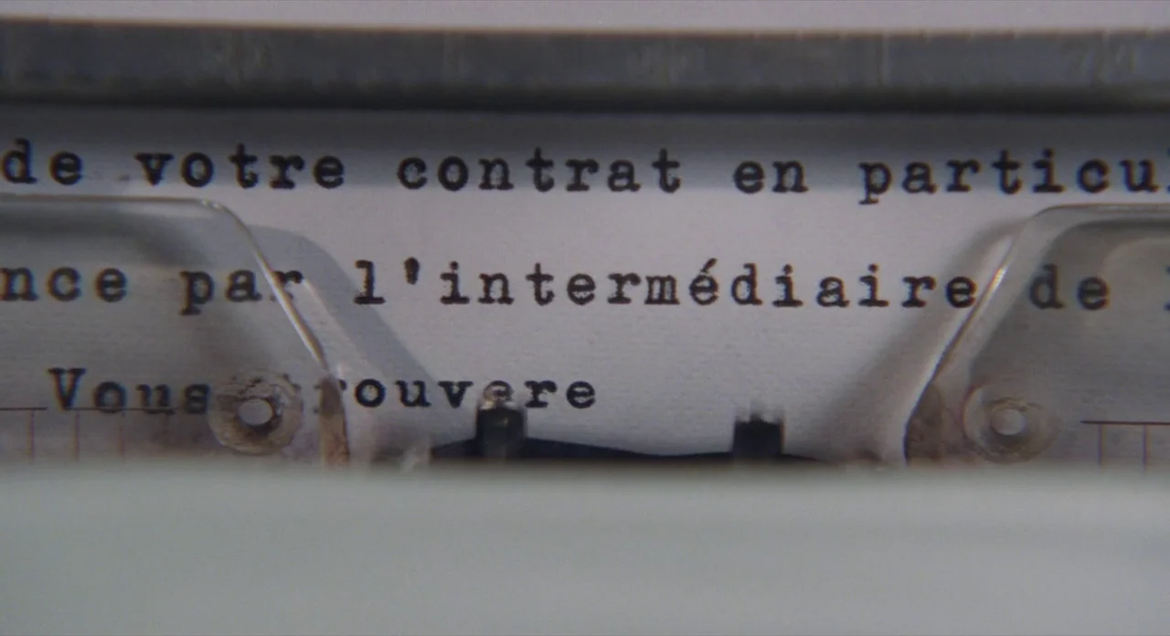 Populaire (2012) movie still: closeup — A close-up view shows a sheet of paper inside a mechanical typewriter. Black ink marks clearly spell out…