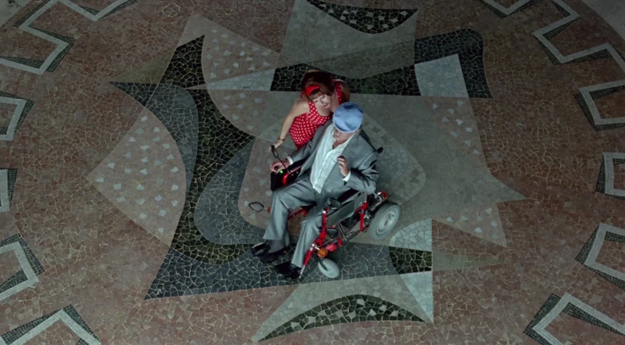Tie Me Up! Tie Me Down! (1989) movie still: wide — A spacious room features a complex geometric mosaic pattern on the ground surface. A man in a…