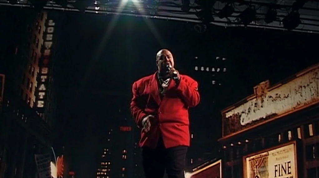 Bamboozled (2000) movie still: medium — A theatrical city street set at night features retro signage and dark urban surroundings. A man in a red…