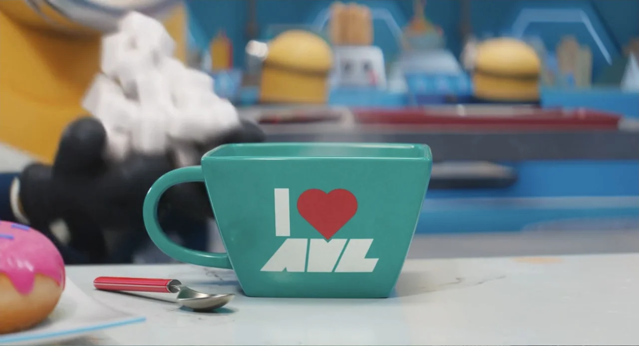 Despicable Me 4 (2024) movie still: closeup — A teal mug with an I Love AVL logo rests on a white table. A pink frosted donut and a small spoon are…
