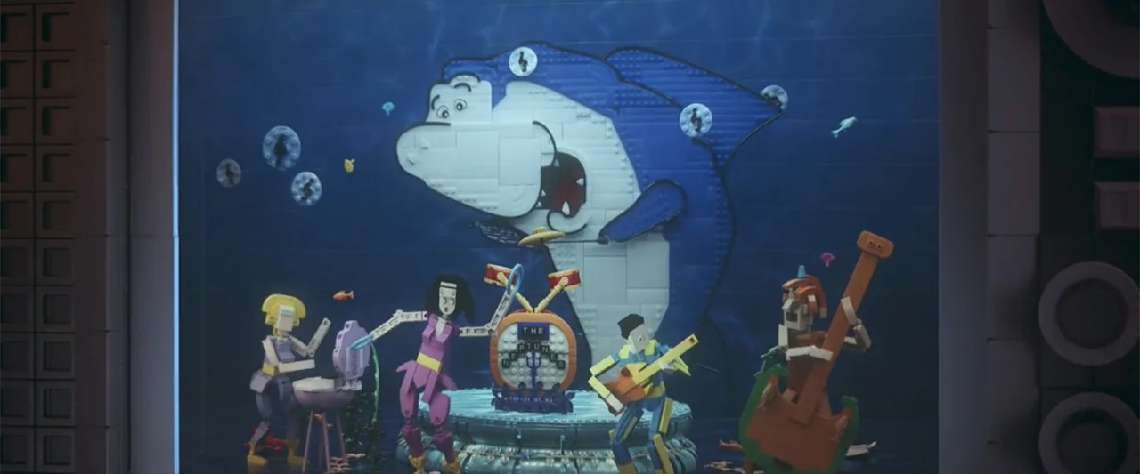 Piece by Piece (2024) movie still: wide — An underwater diorama constructed from colorful plastic bricks features a band of figures. A large…