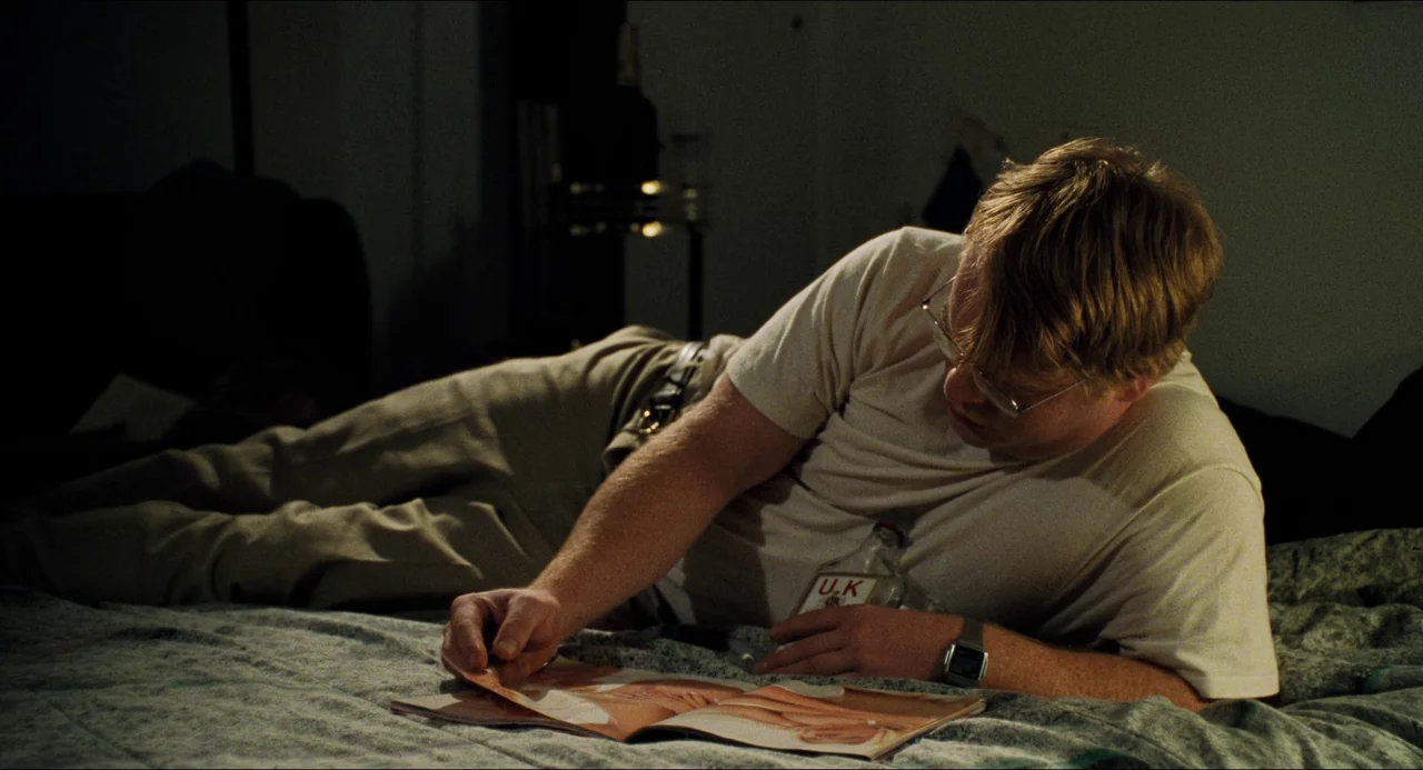 Happiness (1998) movie still: medium — A dimly lit room at night features a man lying on a patterned bedspread. He rests on his stomach while…