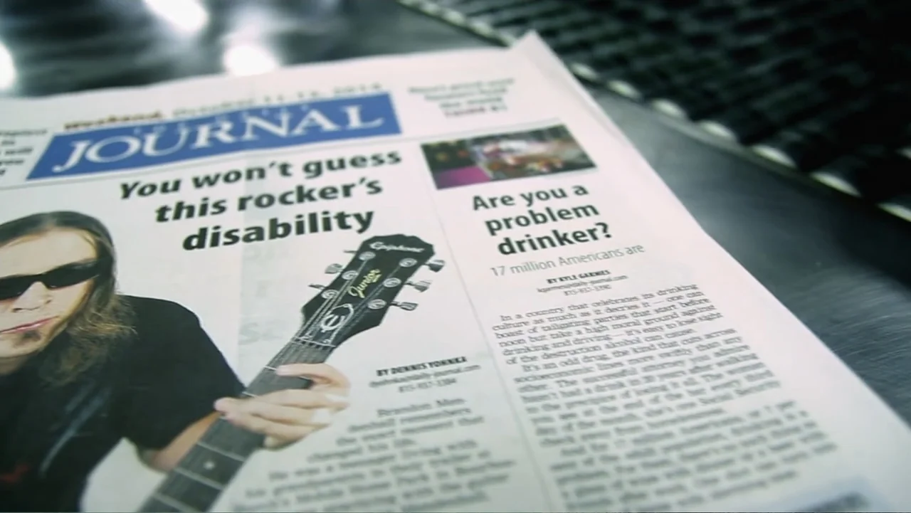 Control (2022) movie still: closeup — A close-up view of a newspaper page featuring an article headline and text. The newspaper is laid flat on a…