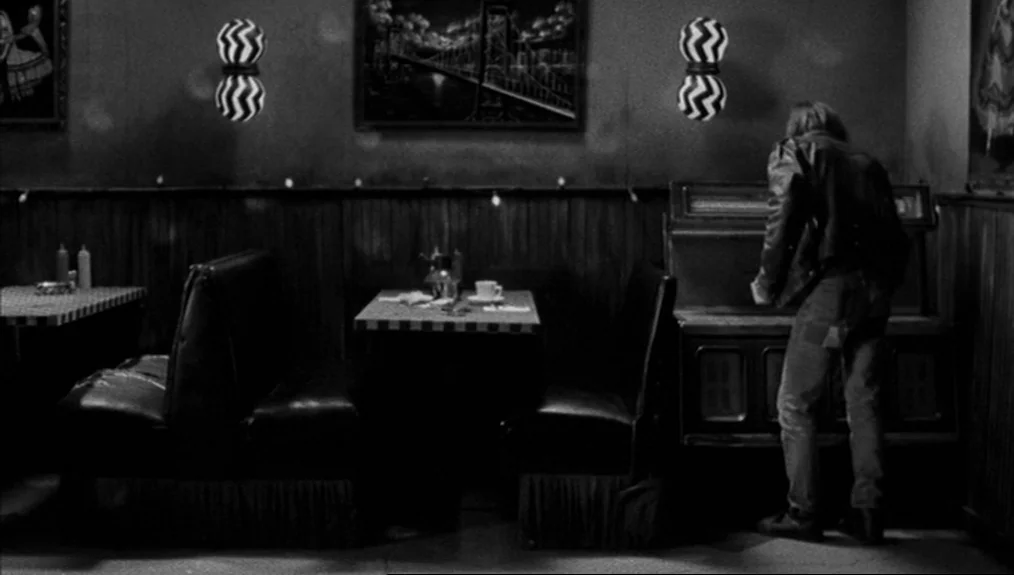 Coffee and Cigarettes (2003) movie still: medium — A dimly lit room features wood-paneled walls and distinctive patterned wall sconces. A person…