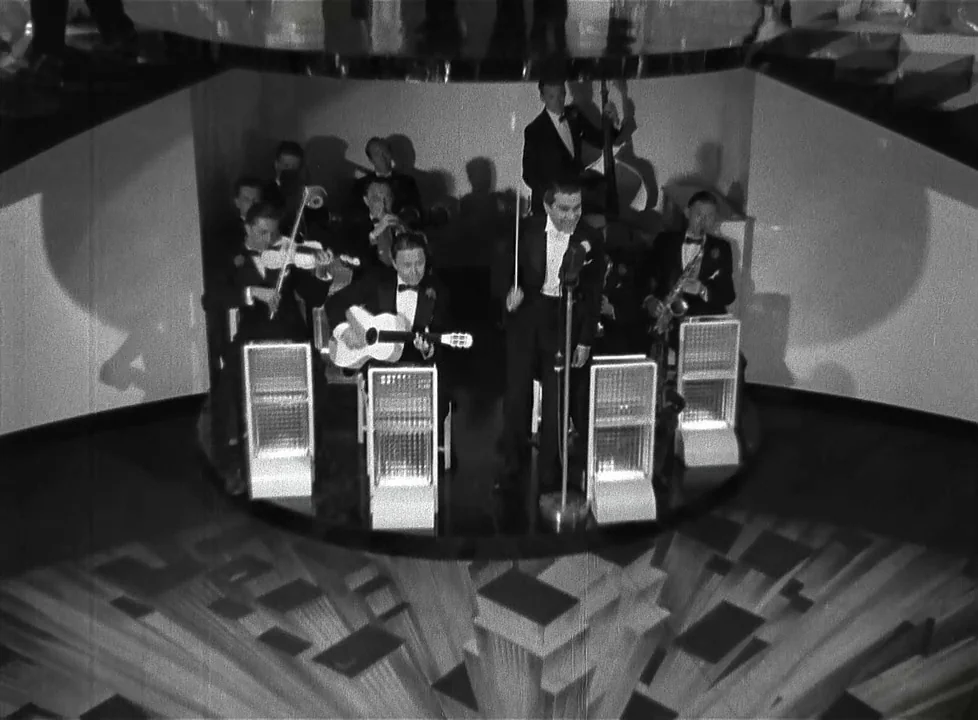 Swing Time (1936) movie still: wide — A jazz orchestra plays on a circular stage with geometric floor patterns and glass panels. The band members in…