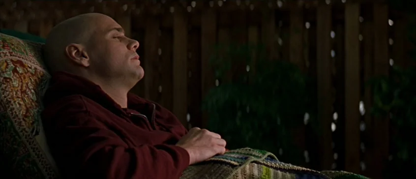 Man On The Moon (1999) movie still: medium — A man lies on a chair on a dark wooden patio at night. He is resting with his eyes closed under a…