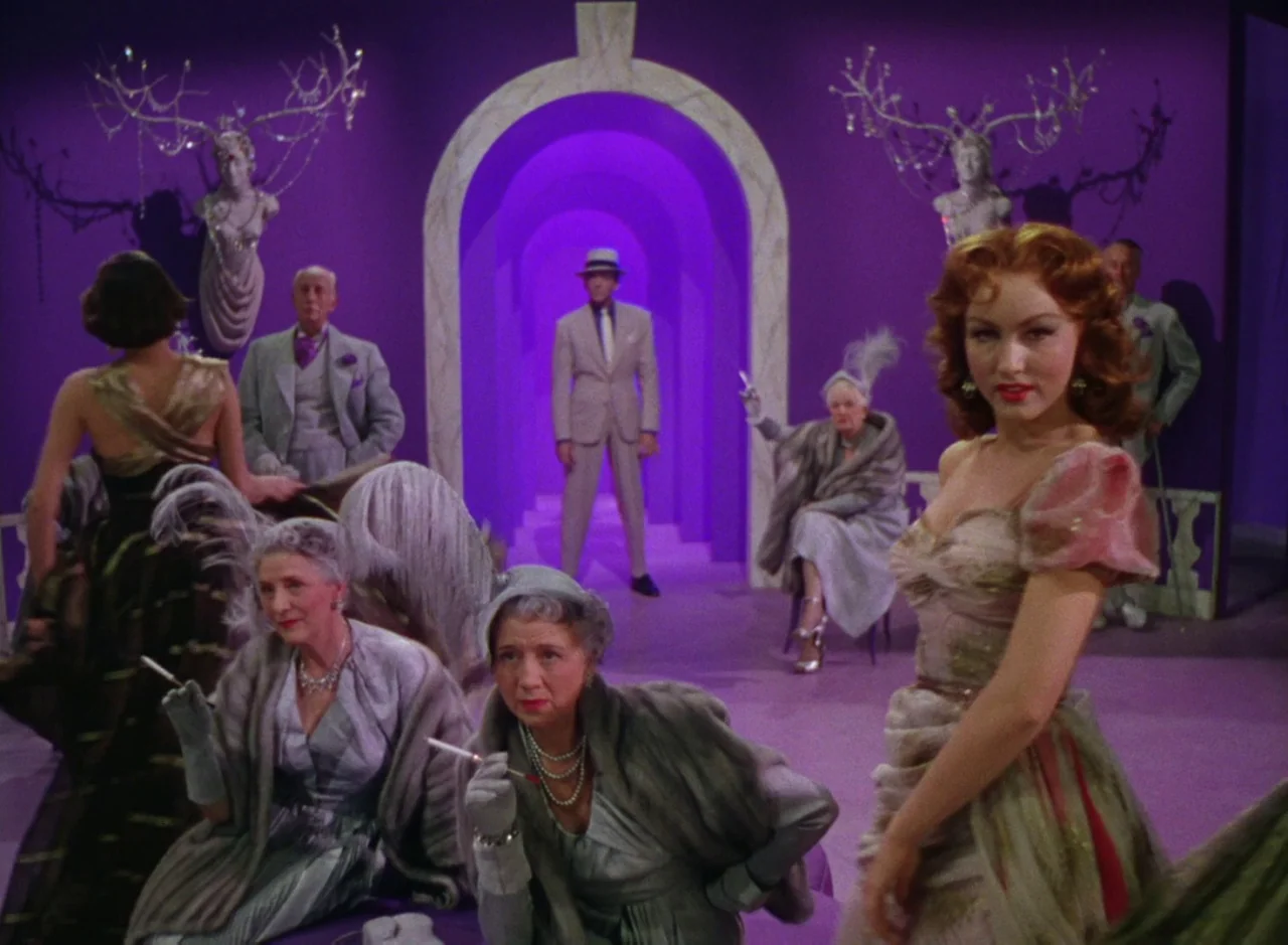 The Band Wagon (1953) movie still: fullbody — A group of people in 1950s evening wear stand in a bright violet ballroom. A woman in a floral dress…