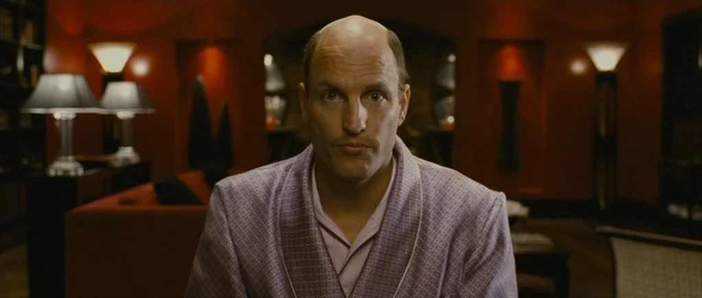 The Walker (2007) movie still: medium — A dimly lit room features red walls and symmetrical lamp arrangements on side tables. A middle-aged man in a…